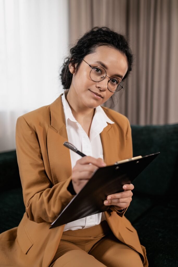 pexels-photo-7642007-7642007 Businesswoman in brown suit sitting on sofa writing notes on clipboard